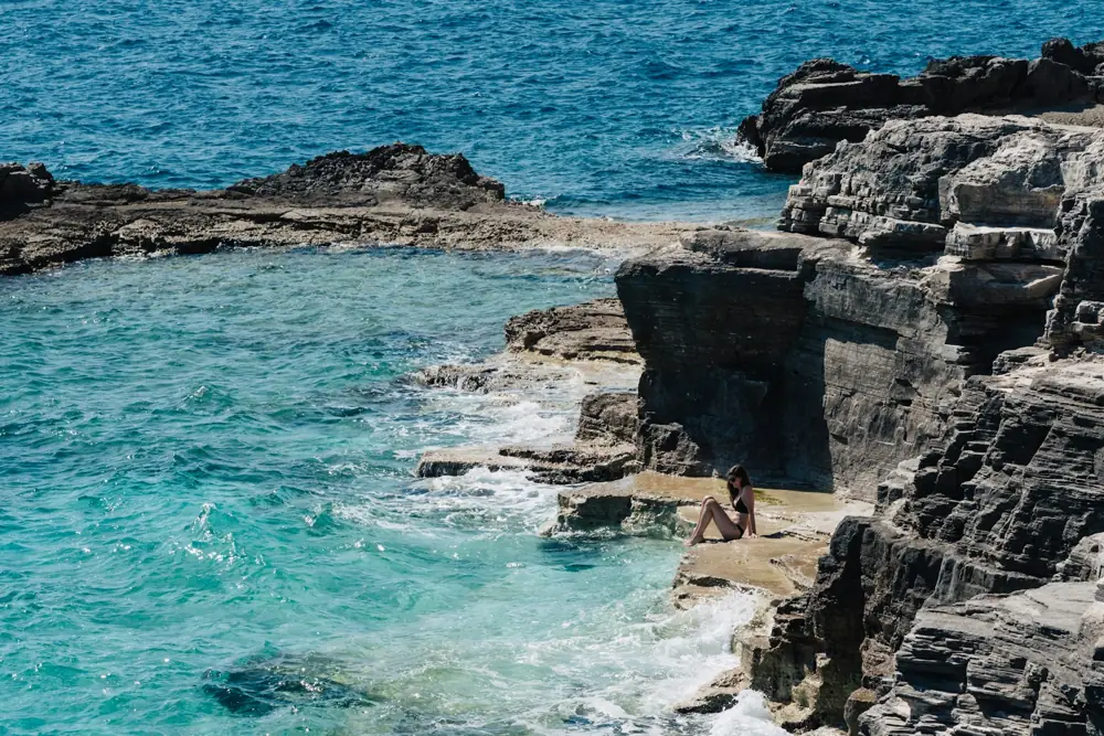 Person sitting on flat limestone rocks beside clear turquoise sea on the Istrian coast