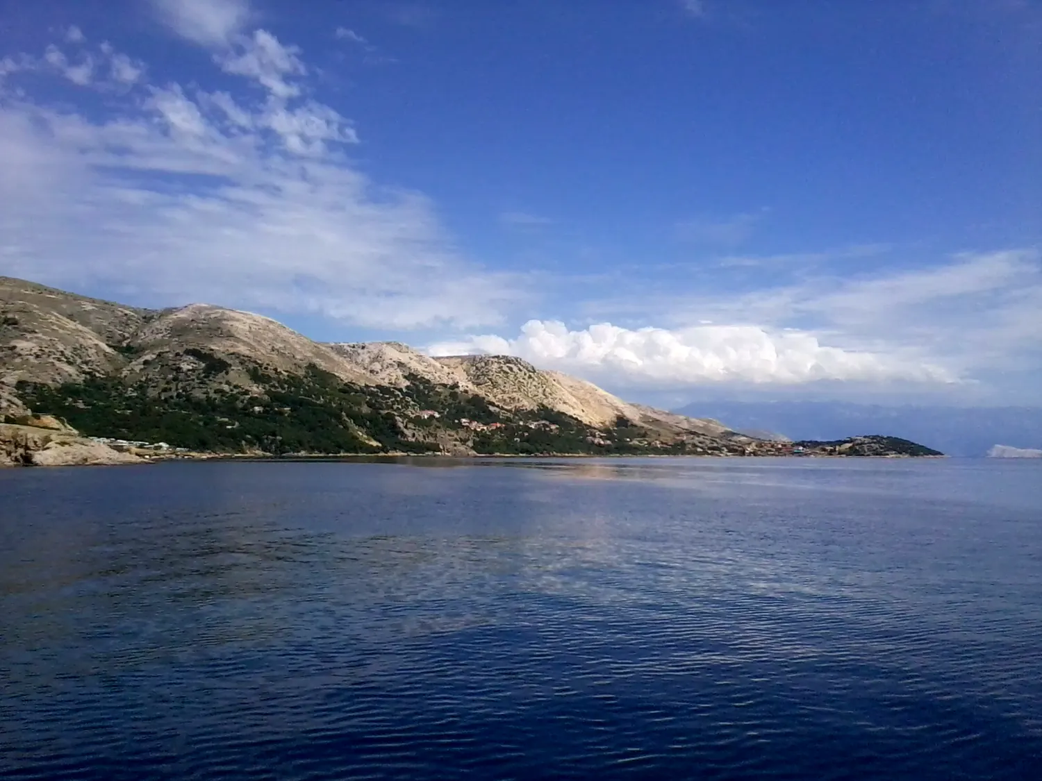Barren limestone hills dropping to calm sea at Stara Baska in the south-west of Krk, Croatia