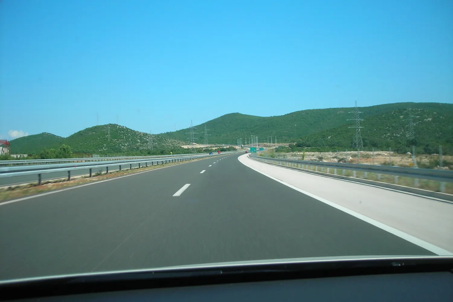 An empty stretch of the A1 motorway running through green hills in Croatia, seen from behind the windscreen