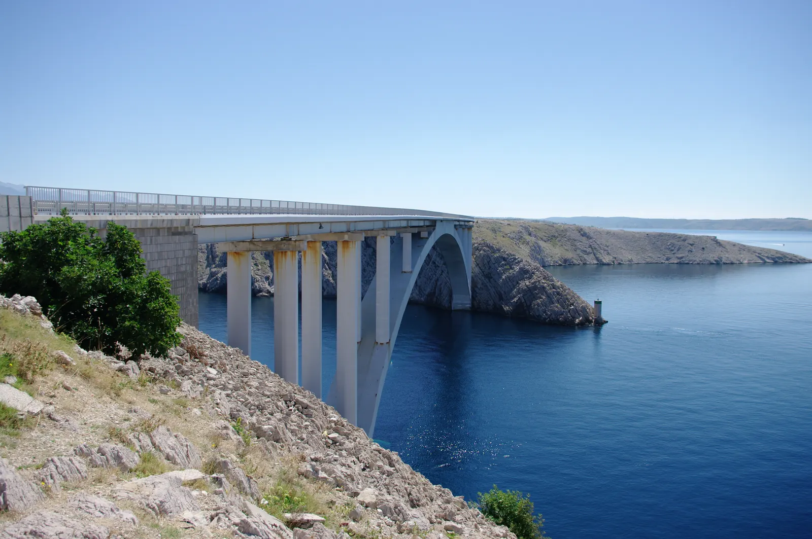 The arched Pag bridge crossing the channel to the island of Pag between bare limestone shores, Croatia