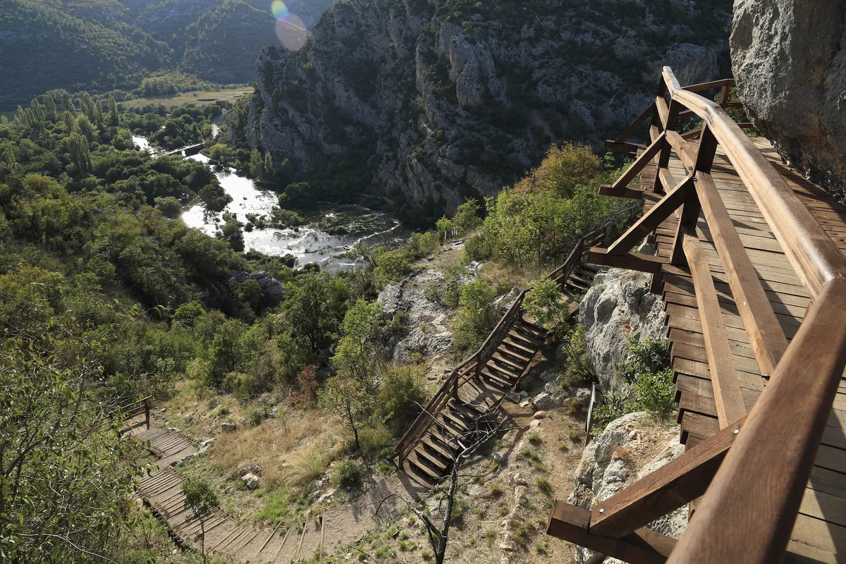 Wooden staircase descending the steep Krka canyon from Oziđana pećina with cascades below at Roški Slap, Croatia